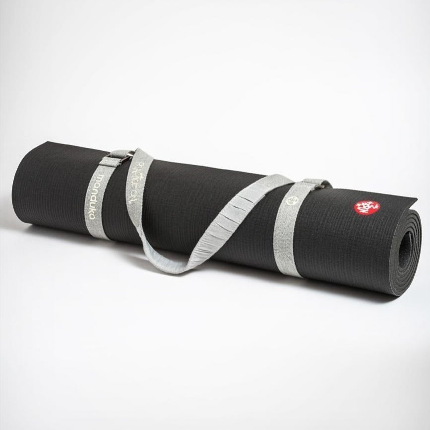 cream colored yoga mat carrier strap fastened around rolled up black manduka yoga mat