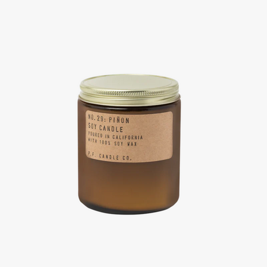 amber glass candle jar with a gold lid and brown label that reads: No. 29: Pinon Soy Candle Poured in California with 100% Soy Wax P.F. Candle. Co.