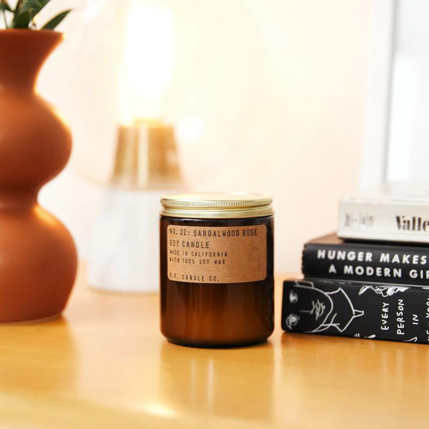 amber glass candle jar with gold lid on table with books and orange planter