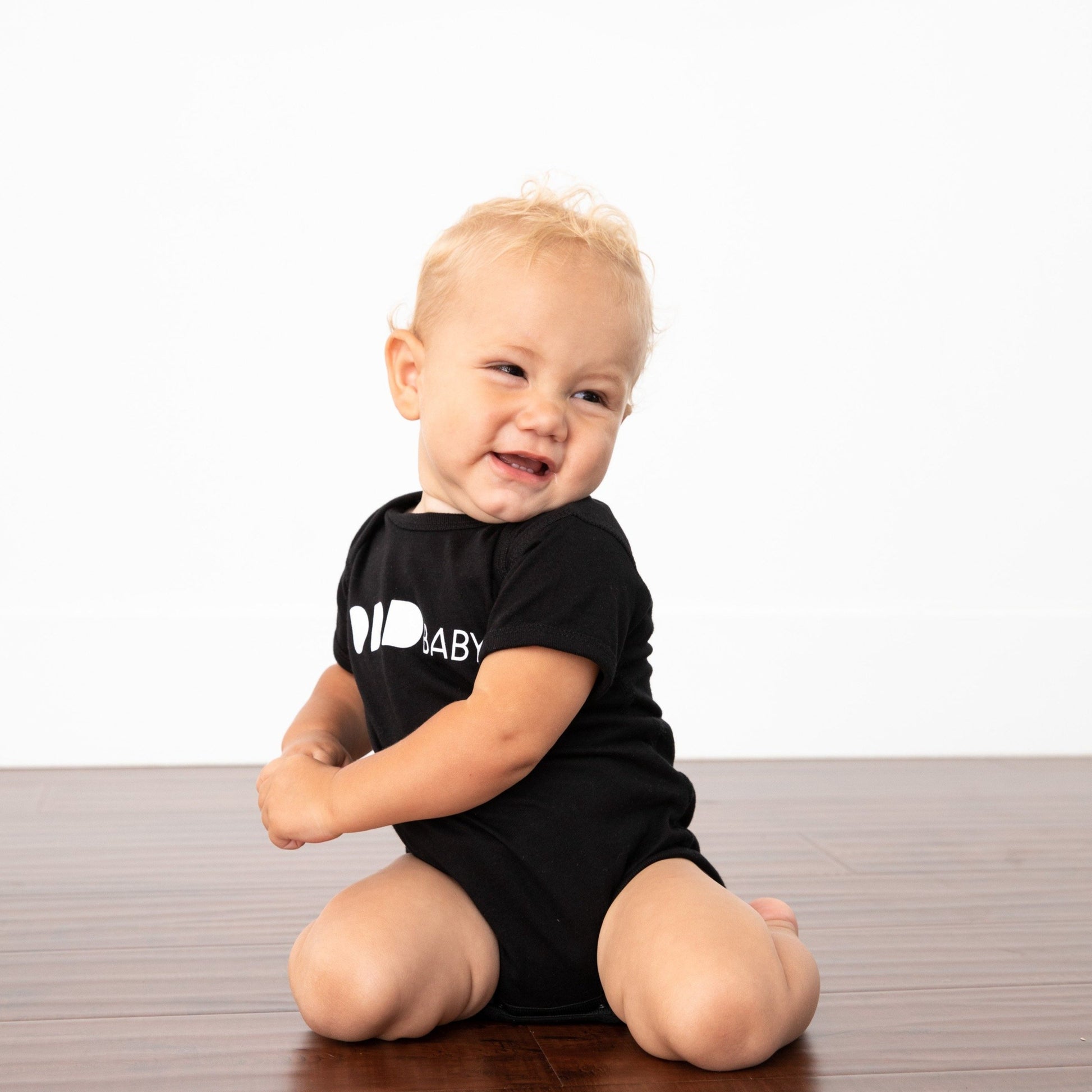 Baby on knees twisting holding hands in black onesie with ODD baby written in white letters