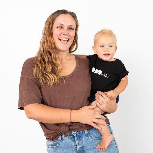 Woman holding baby in black tee with ODD baby written in white letters