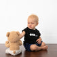Baby sitting next to teddy bear in black tee that says ODD baby in white letters