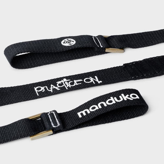 close up of black yoga mat carrier strap with "Practice on" and "manduka" written in white