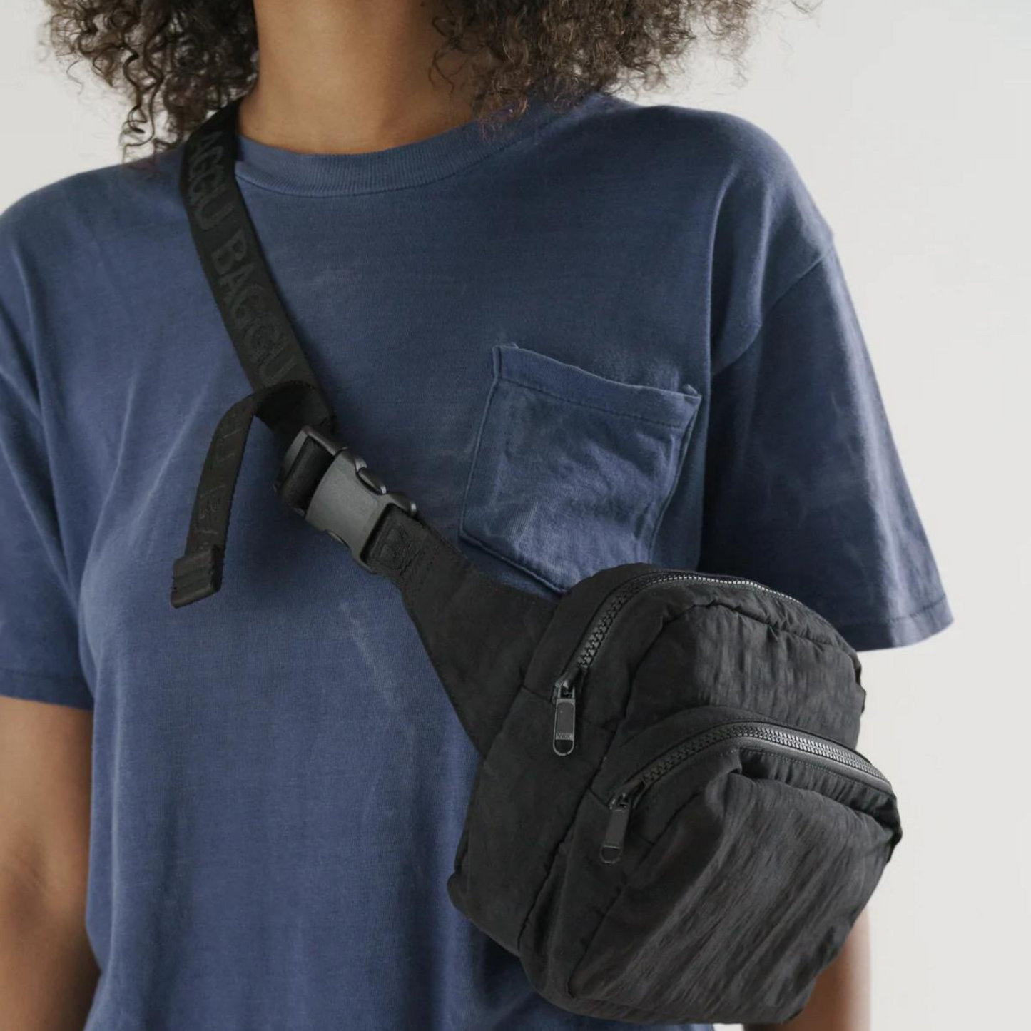 close up of person in a blue tee shirt wearing black fanny pack with two pockets and black strap with buckle