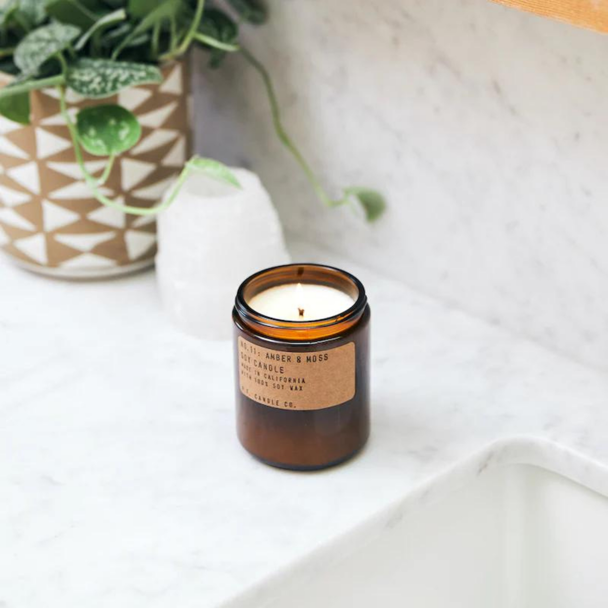 amber jar with lit candle on a marble countertop with a plant in the background