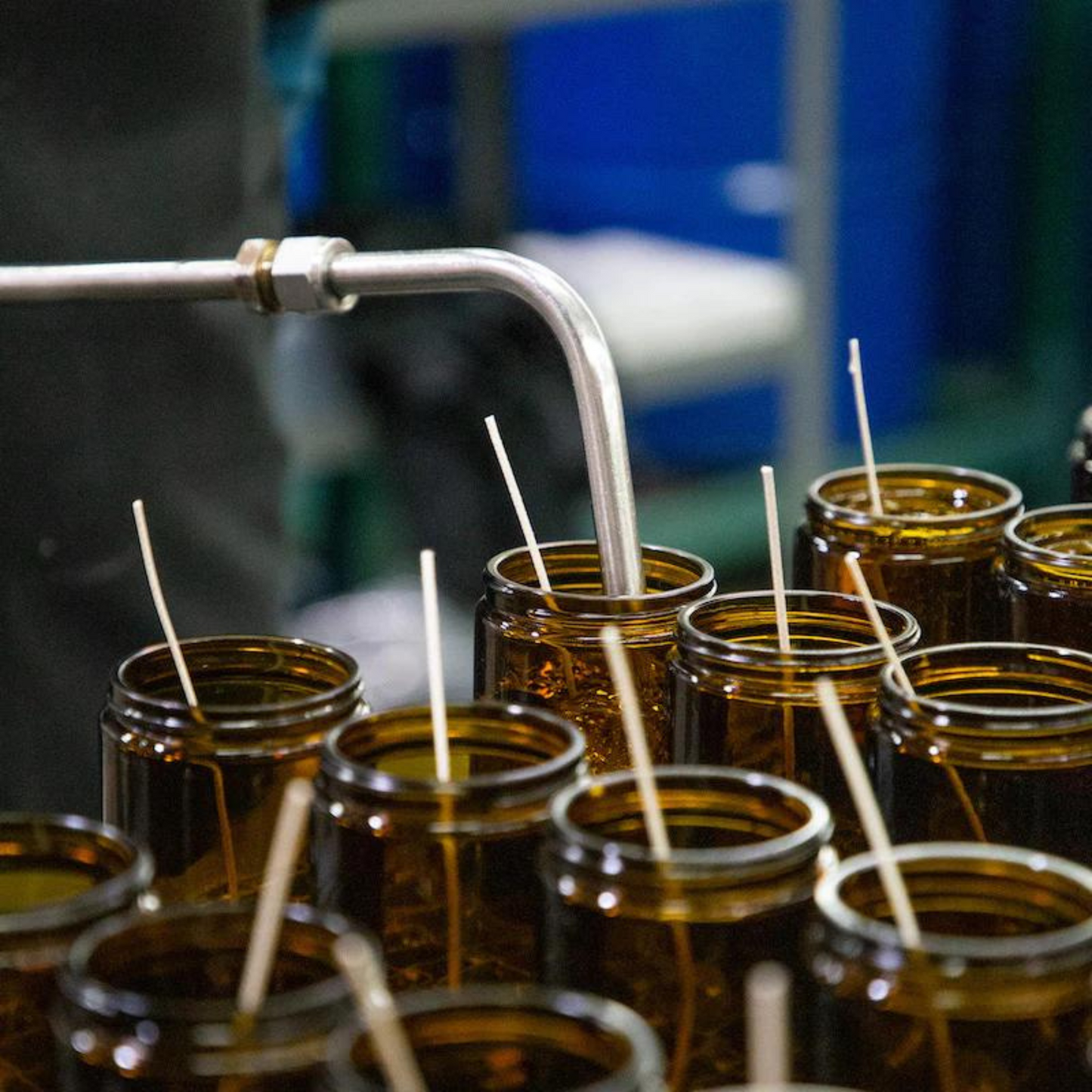 amber glass candle jars with long wicks being filled by a long silver tube