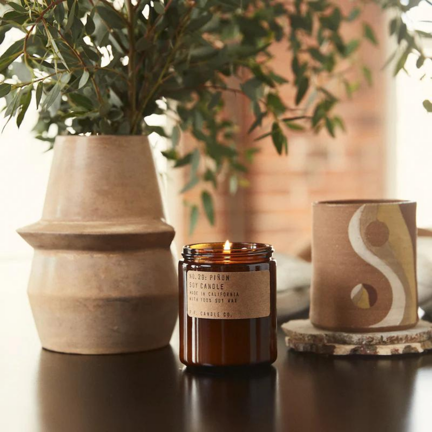 amber glass jar with lit candle on a table with a plant and a ceramic pot